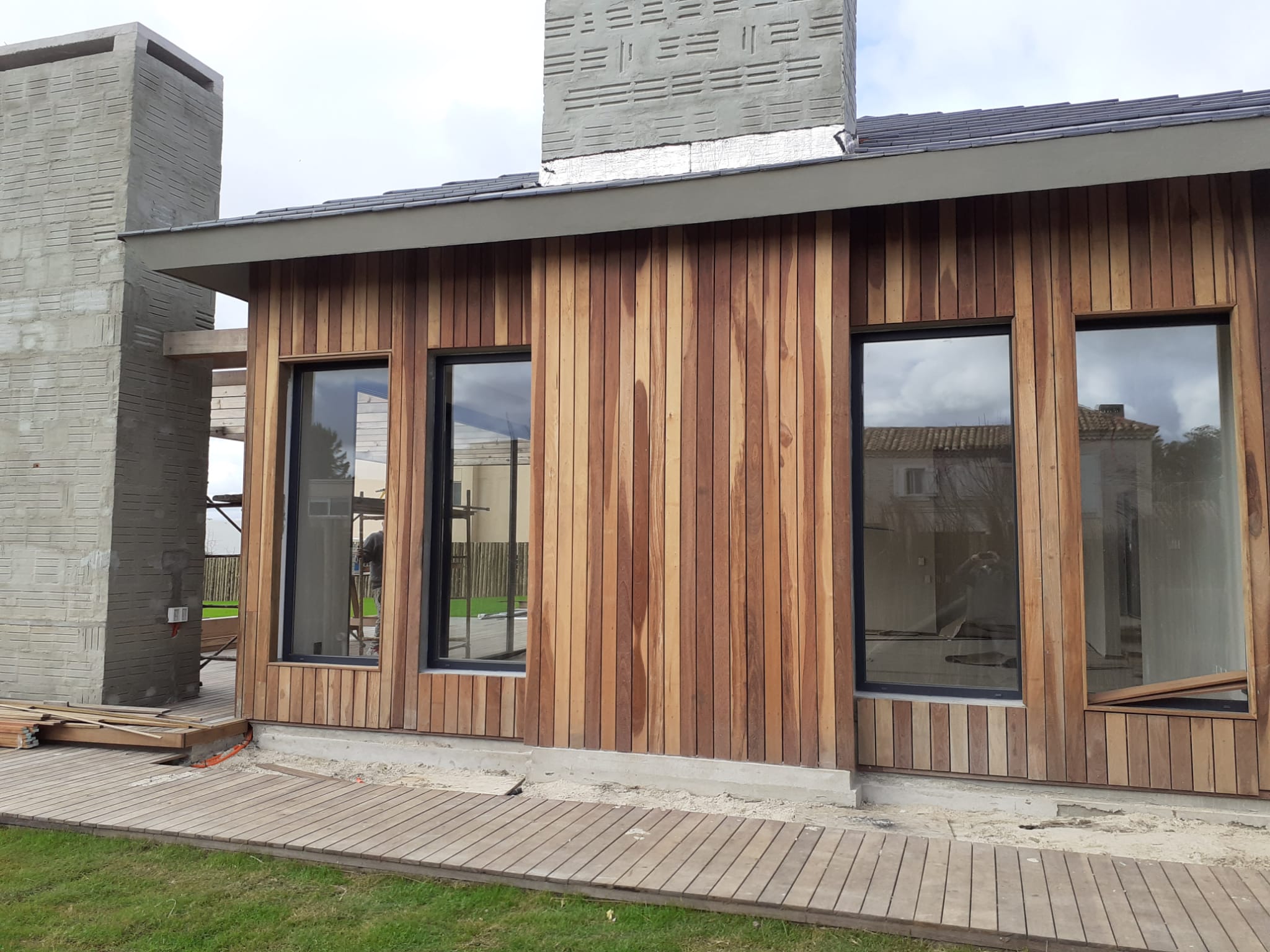 Fachada con revestimiento de madera y ventanales, deck frontal en obra