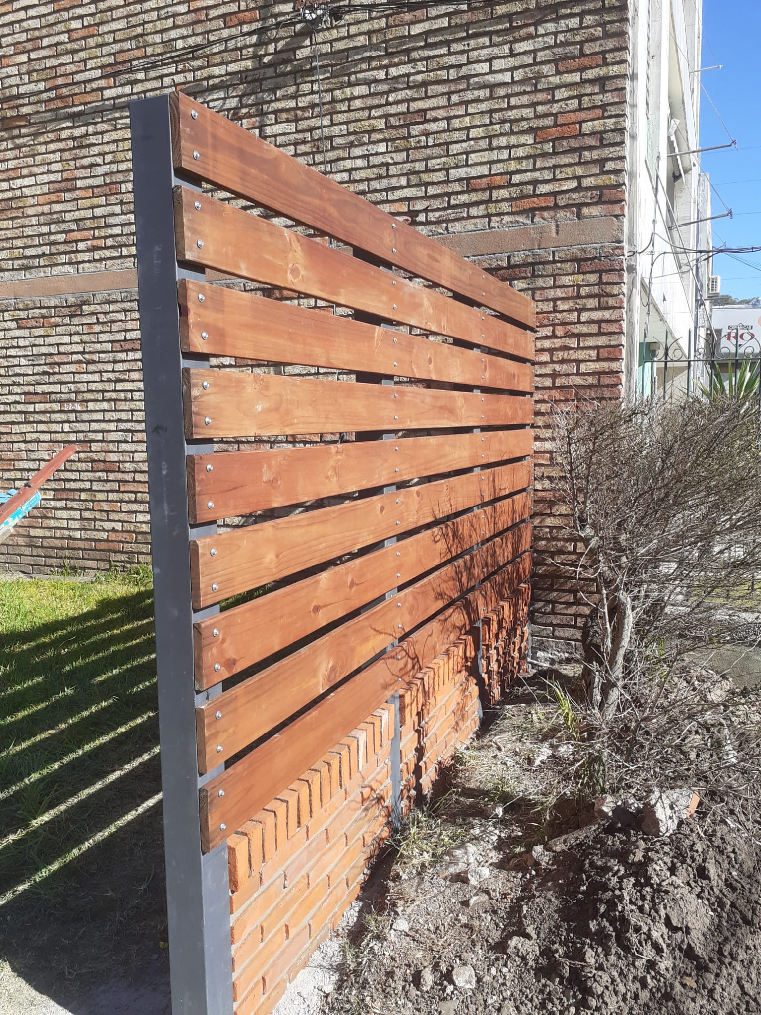 Cerco cortasol de madera y hierro junto a pared ladrillo