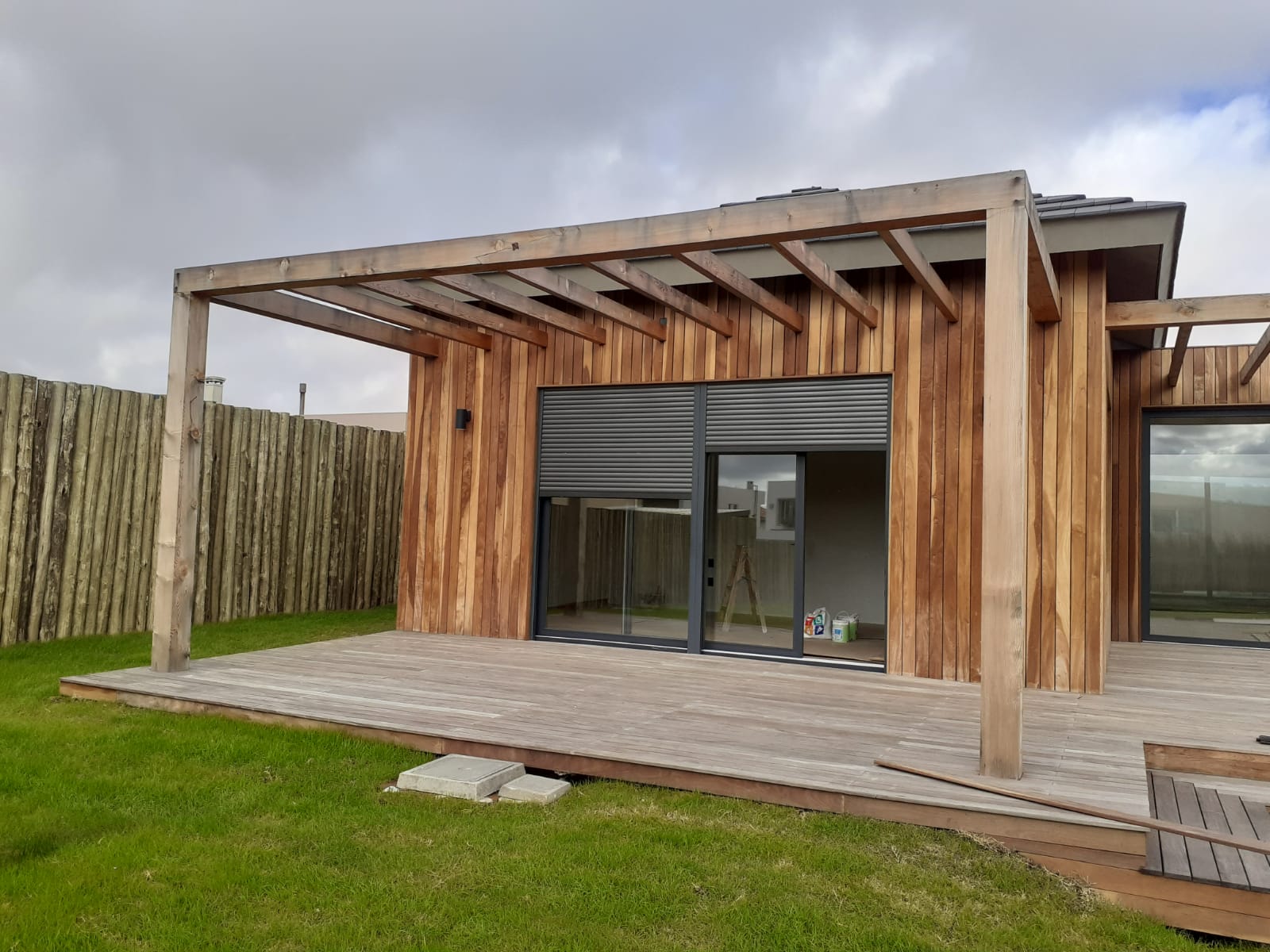 Pergola de madera y deck en fachada de vivienda con cesped