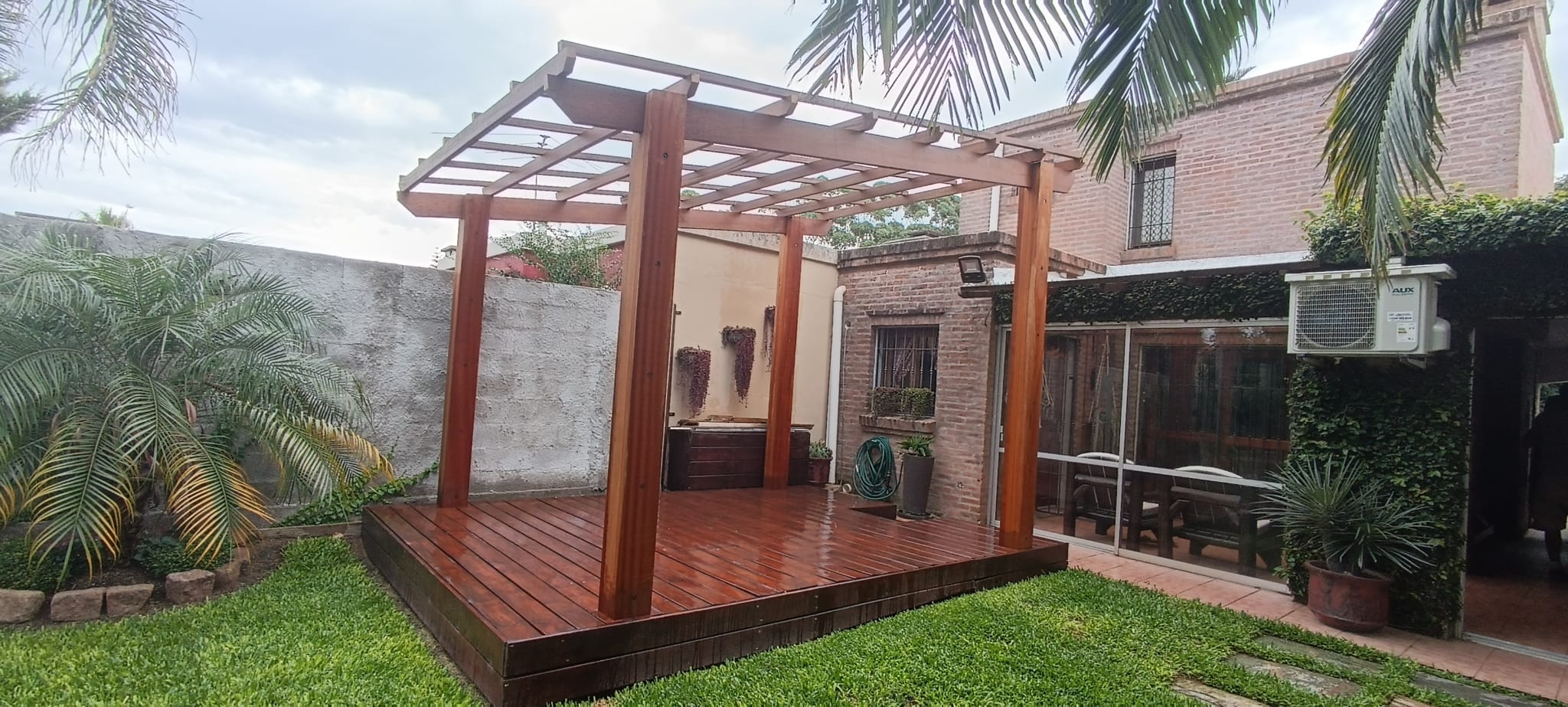 Pérgola de madera sobre deck en jardín junto a la casa