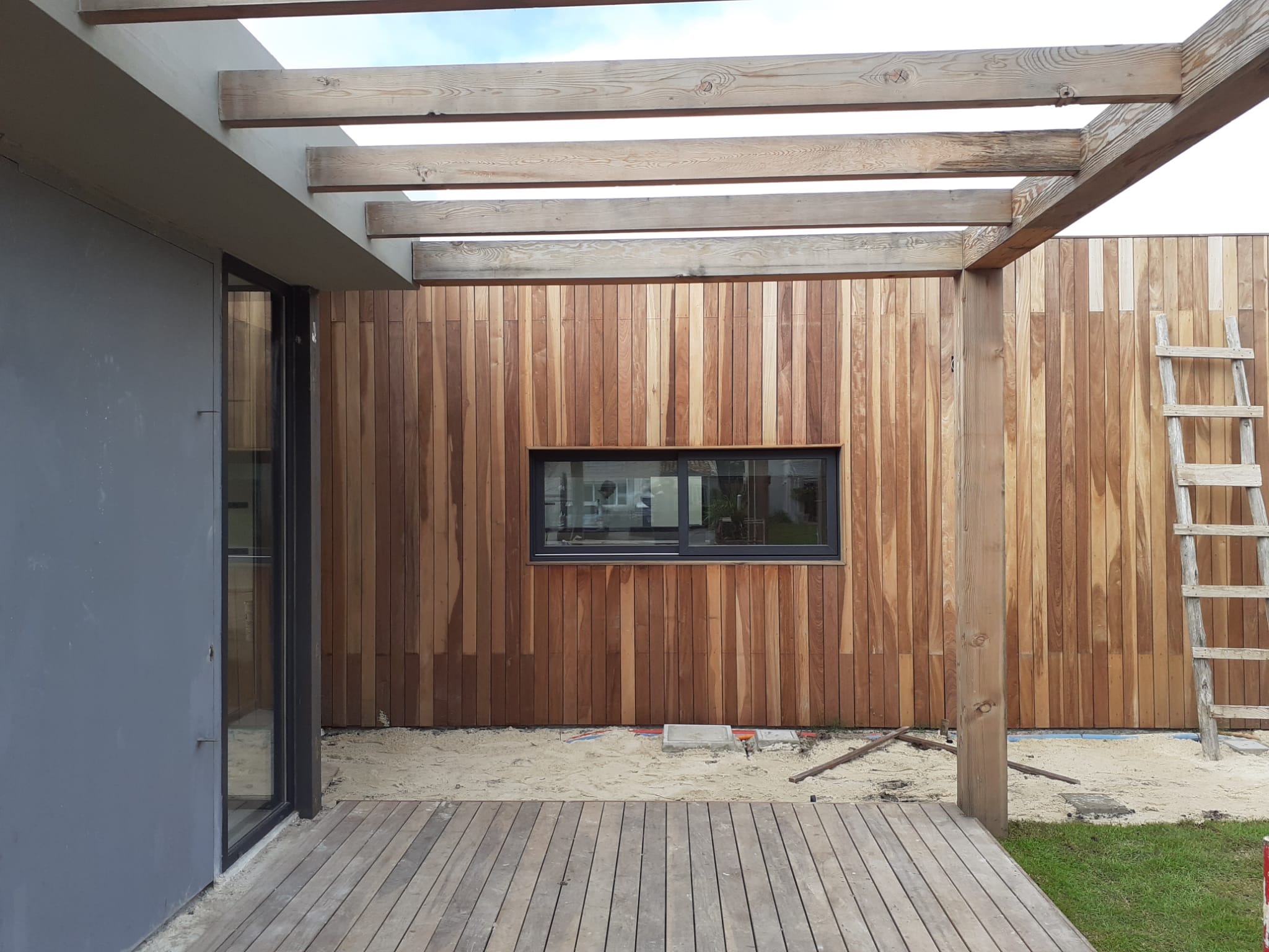 Pergola de madera sobre deck junto a fachada revestida en madera