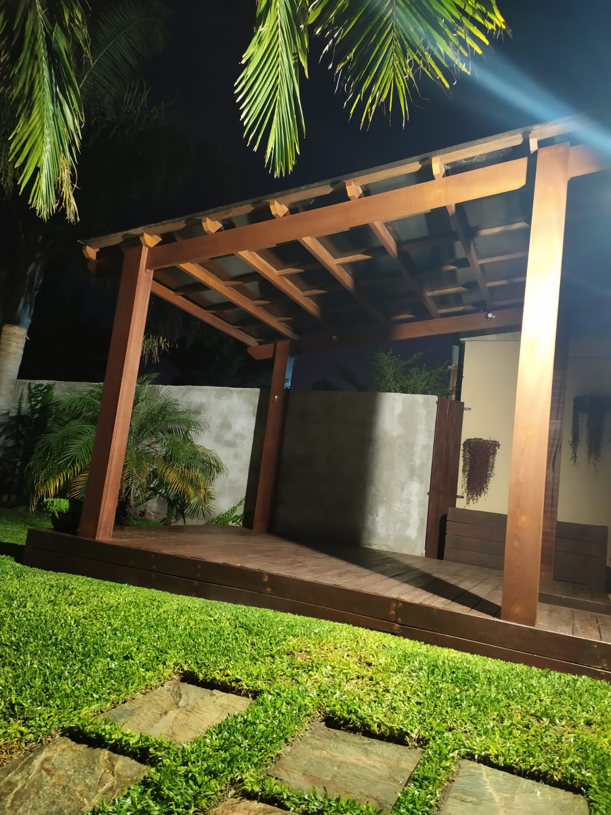 Pérgola de madera iluminada de noche sobre deck, jardín