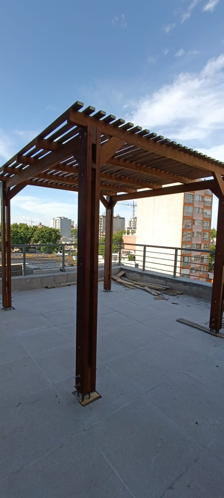 Pérgola de madera sobre terraza con edificios de fondo