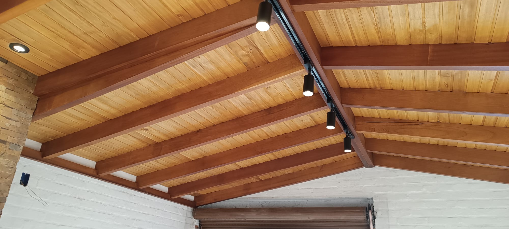 Techo de madera con vigas y luces dirigidas sobre pared blanca