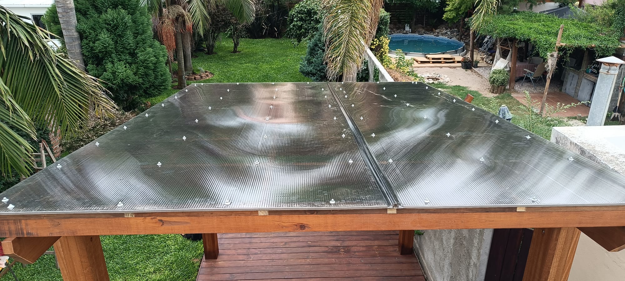 Techo de policarbonato sobre pérgola, piscina y jardín al fondo